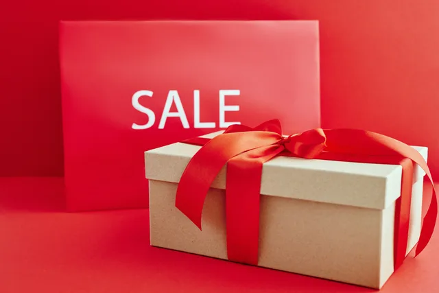 Gift box with red ribbon on red background with sale sign, perfect for retail promotions. Comparing shopping spend with product-level margin