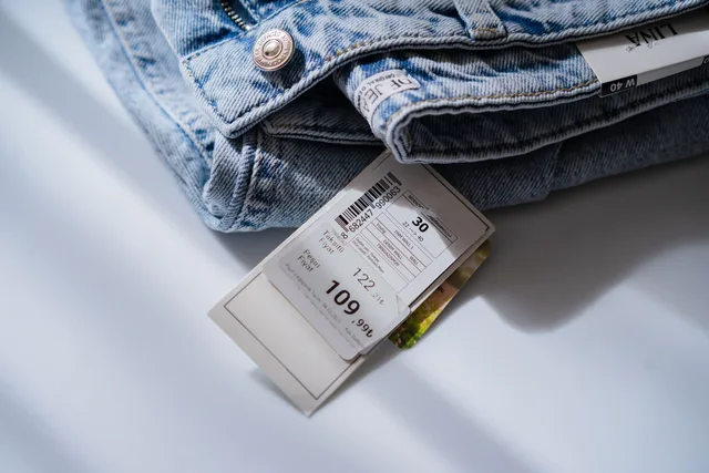 From above of blue jeans with retail price and size label placed on white table. Fixing a mismatch between the ad and the advertised price