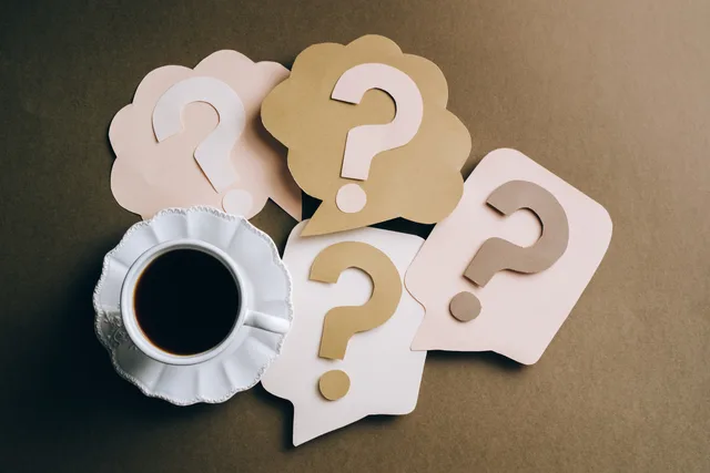 Creative concept with coffee cup and paper question marks on a table. Matching a search ad to a specific buying question
