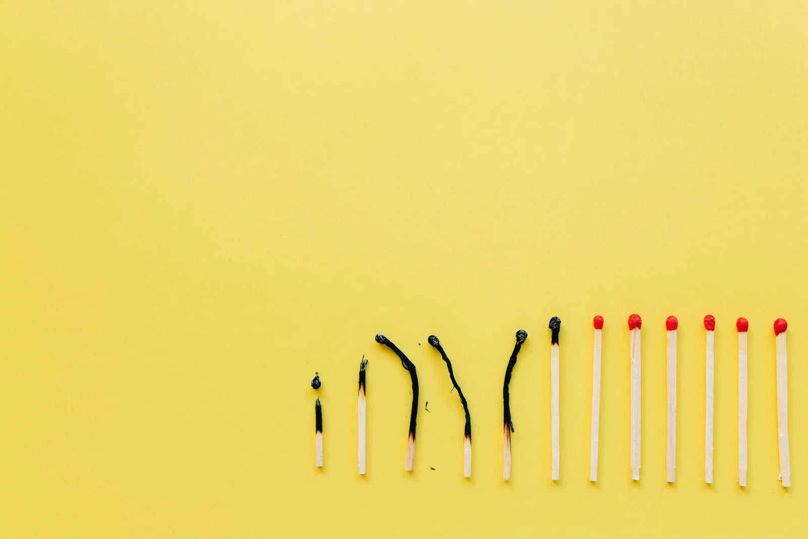 A row of burnt and unburnt matchsticks on a vibrant yellow background illustrating contrast.
