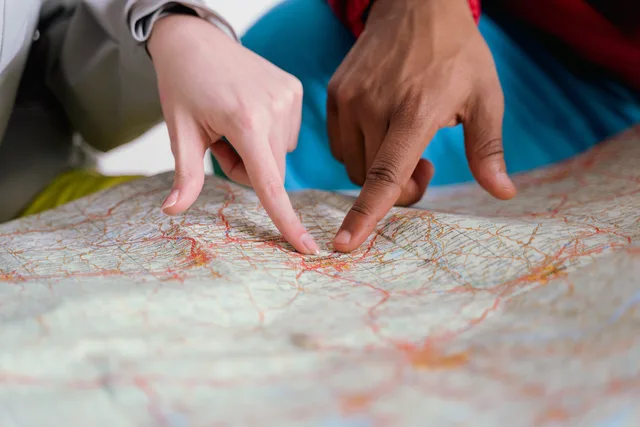 Close-up of diverse hands pointing at a paper map, symbolizing travel planning and navigation. Reviewing location options before launching a local campaign