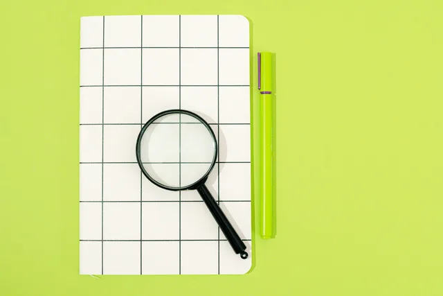 Flat lay of notebook, magnifying glass, and pen on a green background, perfect for office themes. Reviewing search terms without endlessly fragmenting an account