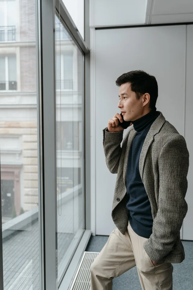 Confident businessman in a gray blazer talking on phone by office window. Tracking call quality from local search ads